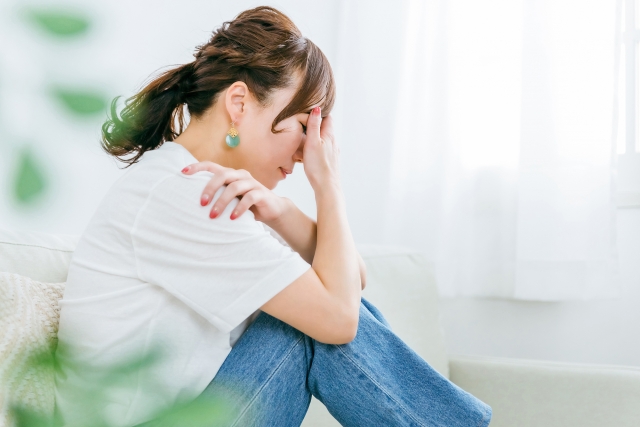 頭痛で頭を抱えて座り込む女性